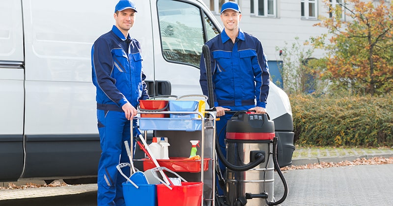 Happy male cleaners standing in front of van with supplies