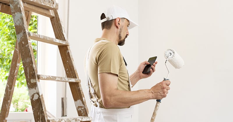 House painter holding mobile phone and paint roller