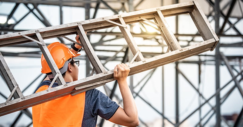 Young man carrying ladder on construction site