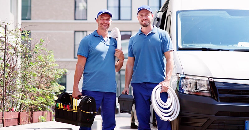 Two plumbers standing infront of van smiling