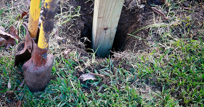 Fence post hole digger and fence post in grass