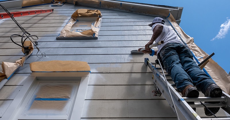 Man stands on ladder painting house exterior