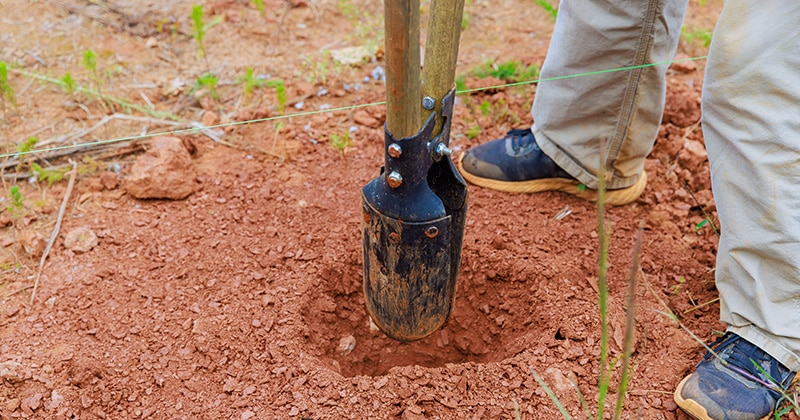Person uses a fence post hole digger in clay