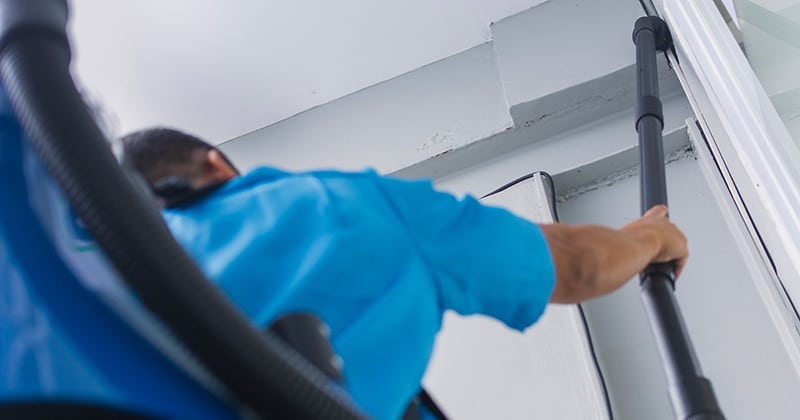 Cleaning professional using backpack vacuum cleaner to clean corner of ceiling in office
