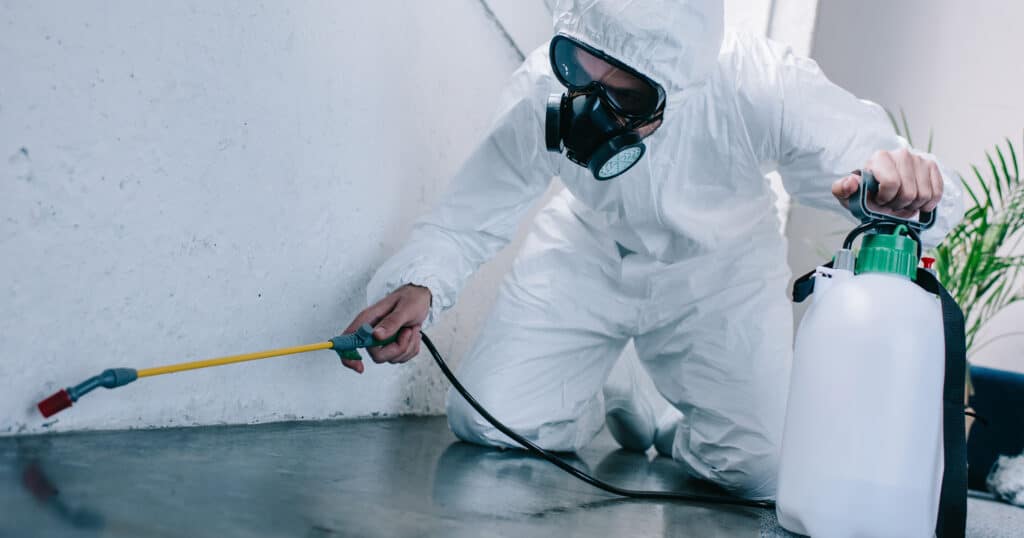 Person in white uniform kneeling while spraying for pests