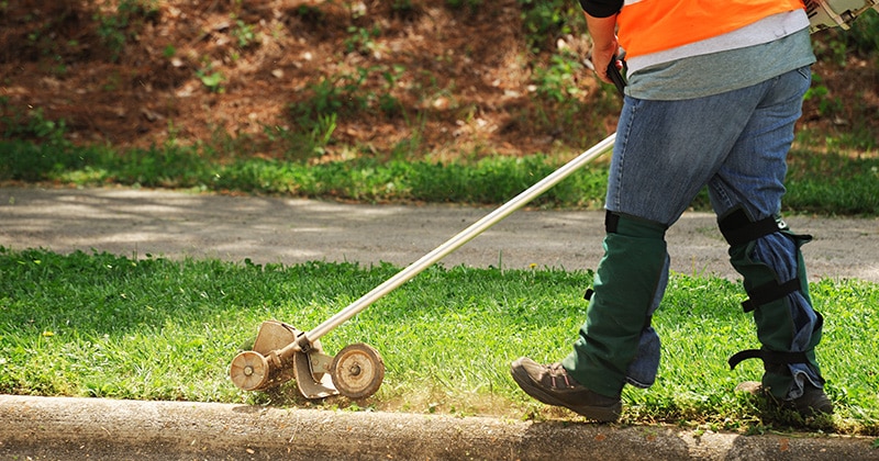 Worker using stick edger next to curb