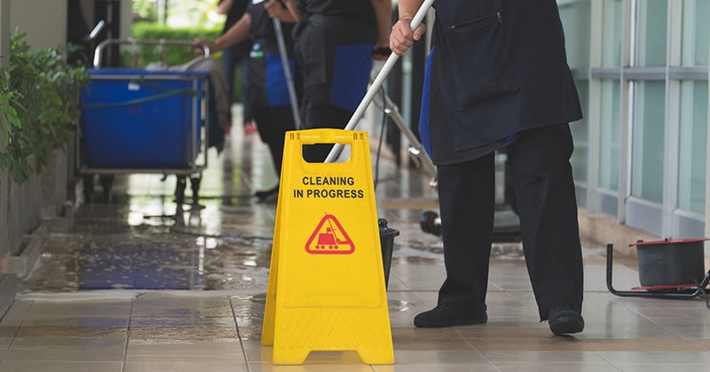 team mopping a floor with a cleaning sign in front