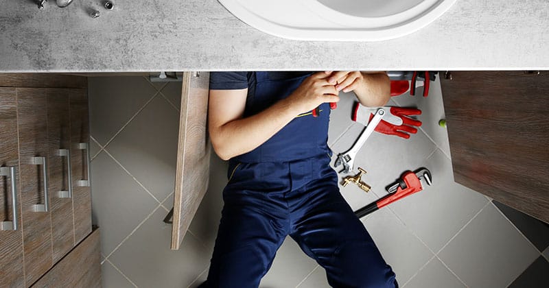 Plumber working under sink surrounded by tools