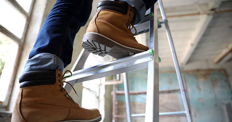 Construction worker in boots climbing metal ladder