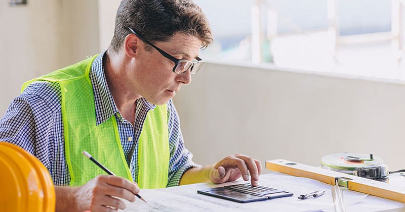 Construction manager sitting at desk using calculator