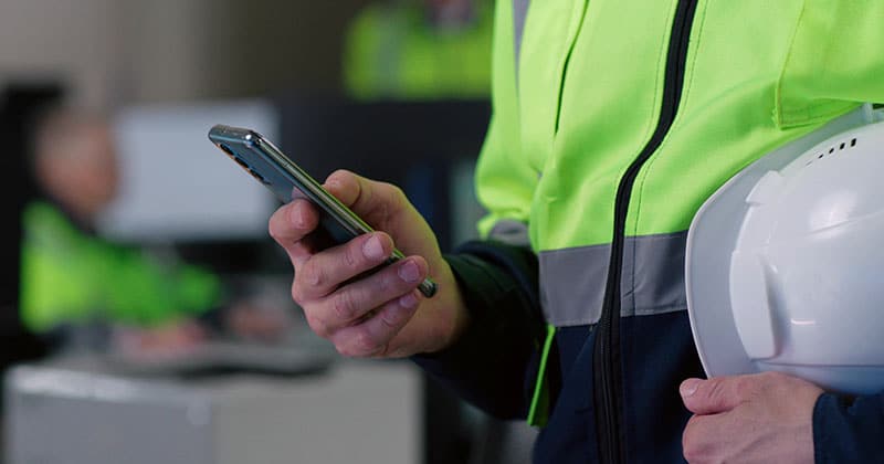 Cropped shot of contractor on smartphone holding hardhat