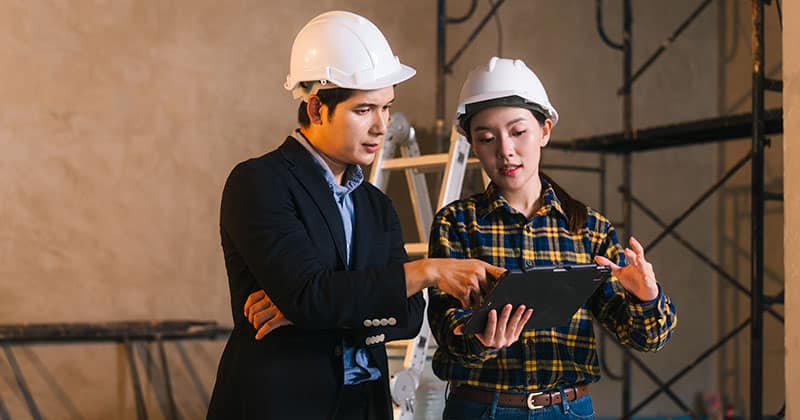Two construction engineers in hard hats reviewing material costs