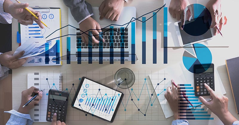 Top-down view of a group of businesspeople working on construction forecasting with laptops, charts, and calculators